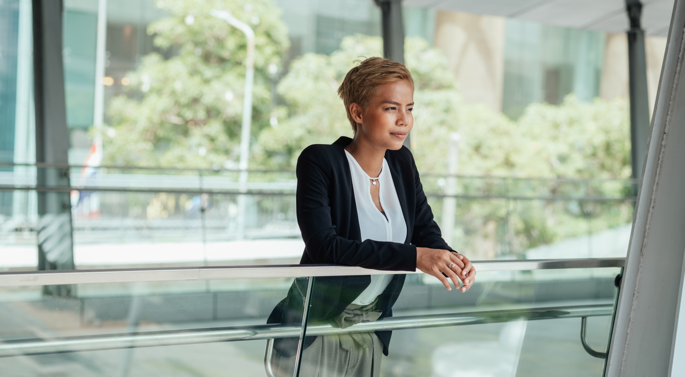 Successful businesswoman leaning on glass railing on a modern office balcony